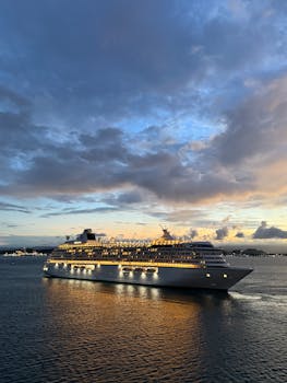 A majestic cruise ship sails on the open sea under a dramatic sunset sky, reflecting golden hues.