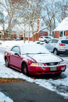 A red car covered with snow parked on a suburban street in Toronto during winter.