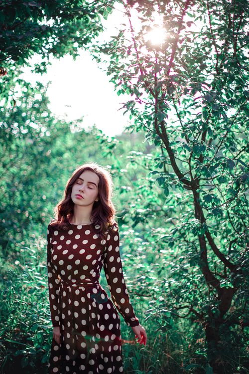 Free Young woman in a vintage polka dot dress enjoying the sunlight in a lush, green forest setting. Stock Photo