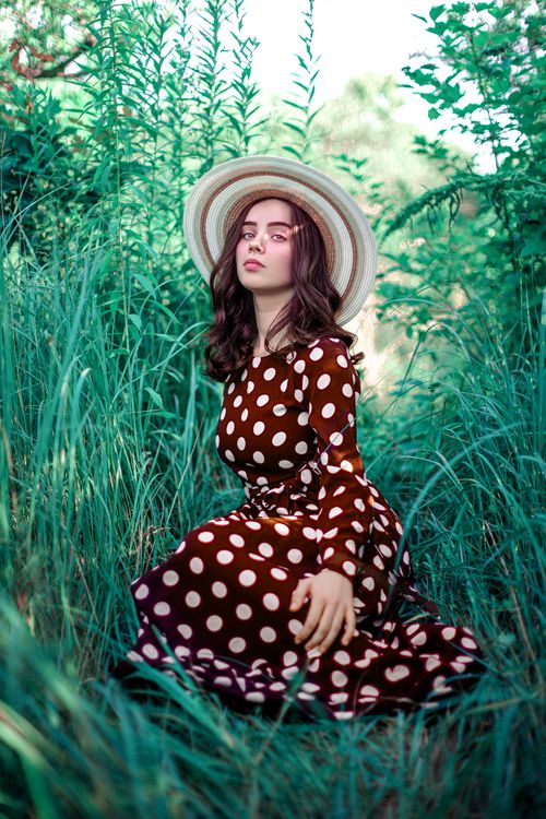 Free Stylish woman in a polka dot dress amidst vibrant summer greenery, embodying vintage charm. Stock Photo