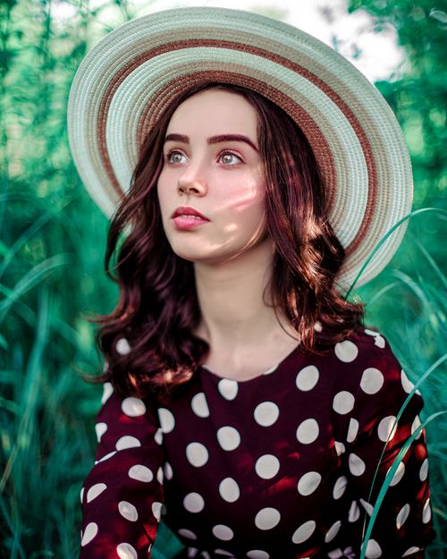 Free A captivating portrait of a woman in a polka dot dress and wide-brimmed hat amidst lush greenery. Stock Photo