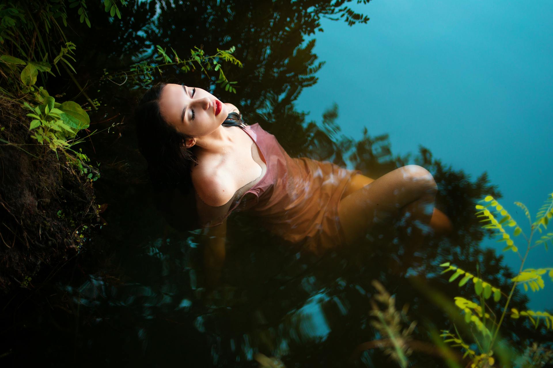 A woman peacefully floating in a river surrounded by lush greenery, creating a tranquil scene.