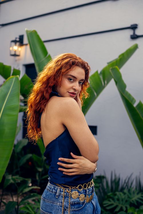 Free Stylish young woman with curly hair poses in an outdoor setting with lush greenery. Stock Photo