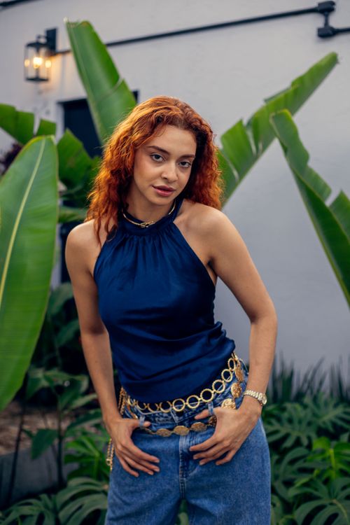 Free Woman with red hair in a blue top stands amidst lush tropical leaves. Stock Photo