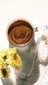 Top view of a coffee cup with foam art beside yellow flowers casting shadows.