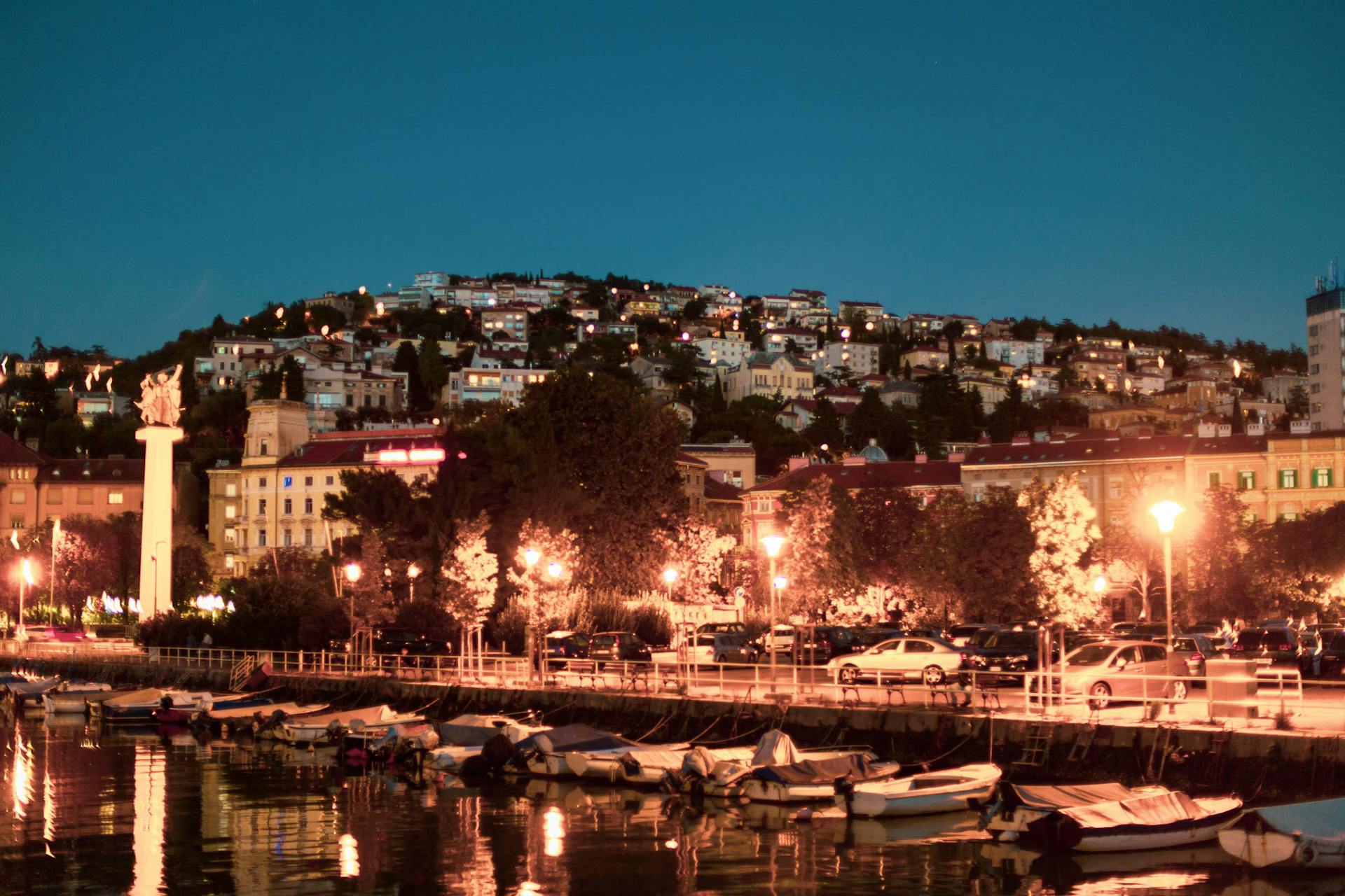 A vibrant night view of the waterfront in Rijeka, Croatia, with boats and city lights.