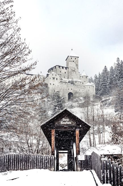 Snowy scene of medieval Burg Taufers Castle surrounded by trees.