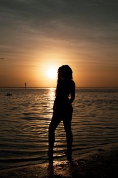 A woman's silhouette standing by the ocean during a vibrant sunset.