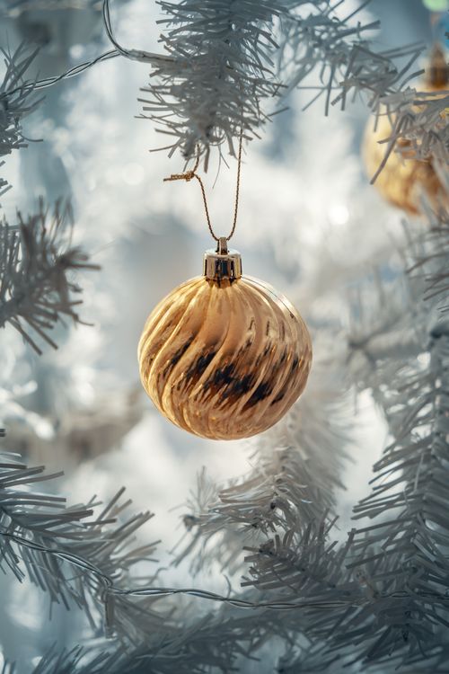 Free Gold Christmas ornament hanging from a white tree branch with soft background lights. Stock Photo
