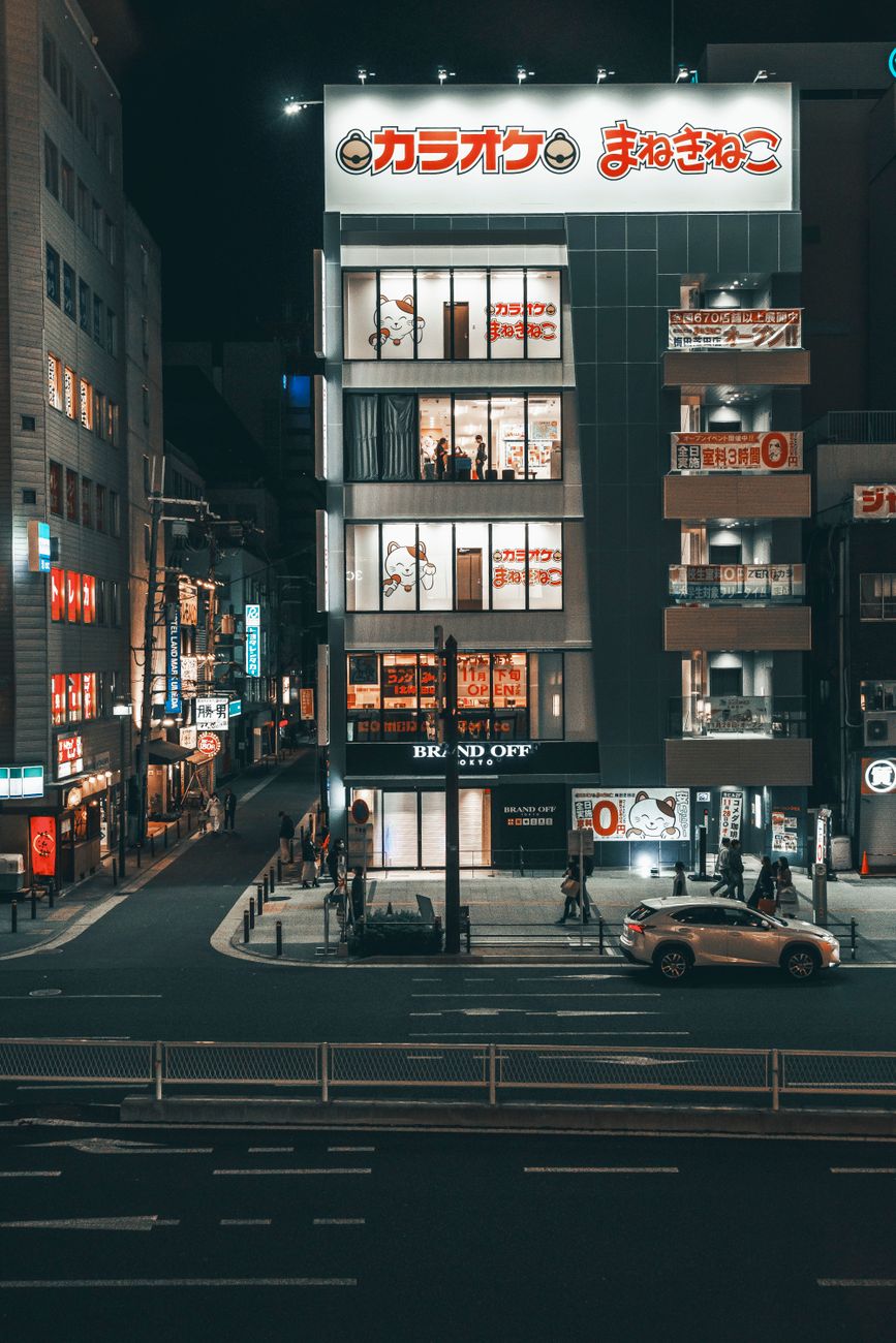 Japanese street at night featuring a karaoke building with neon lights and a bustling atmosphere.
