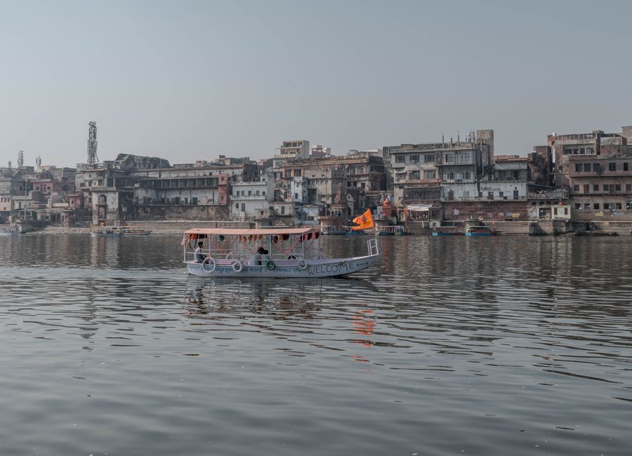 Boat cruising on the Yamuna River with Mathura cityscape in Uttar Pradesh, India.