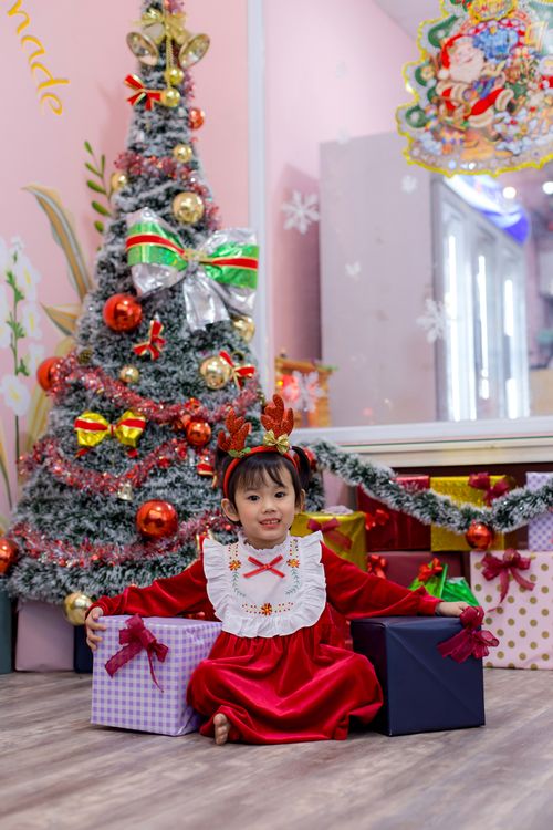 Free A joyful child dressed in red sits amidst Christmas decorations and gifts in Hội An, Vietnam. Stock Photo