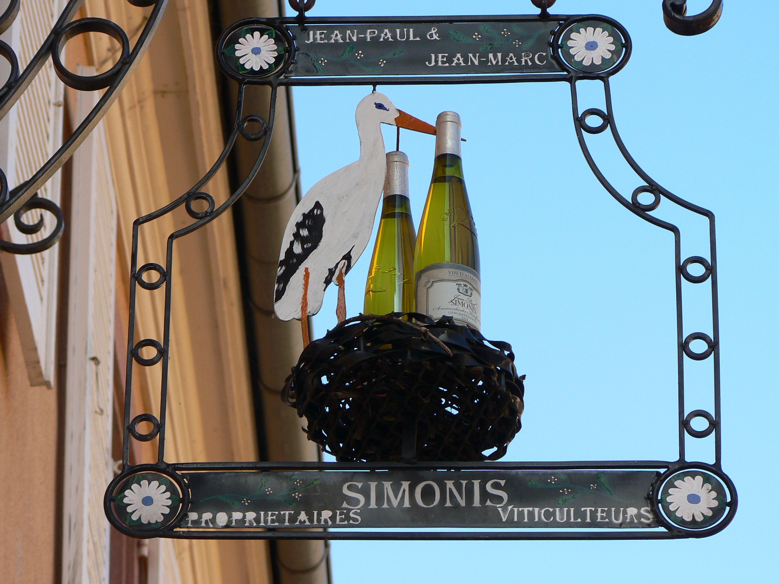 Elegant wine shop sign featuring a stork holding wine bottles in a nest.