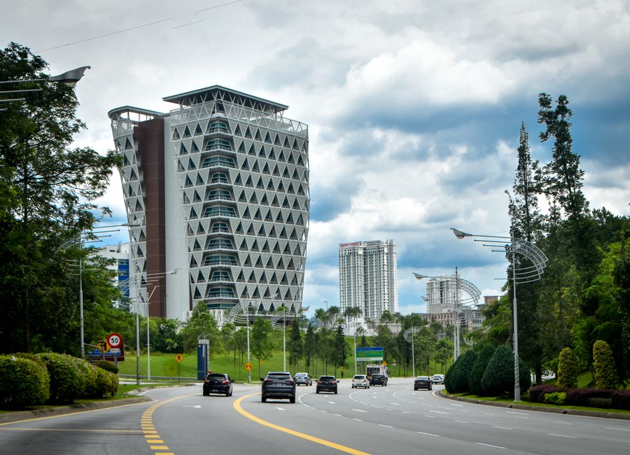 A striking geometric building alongside a roadway with cars, set against a cloudy sky.