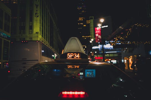 A New York taxi navigates the vibrant city streets at night, surrounded by urban lights.