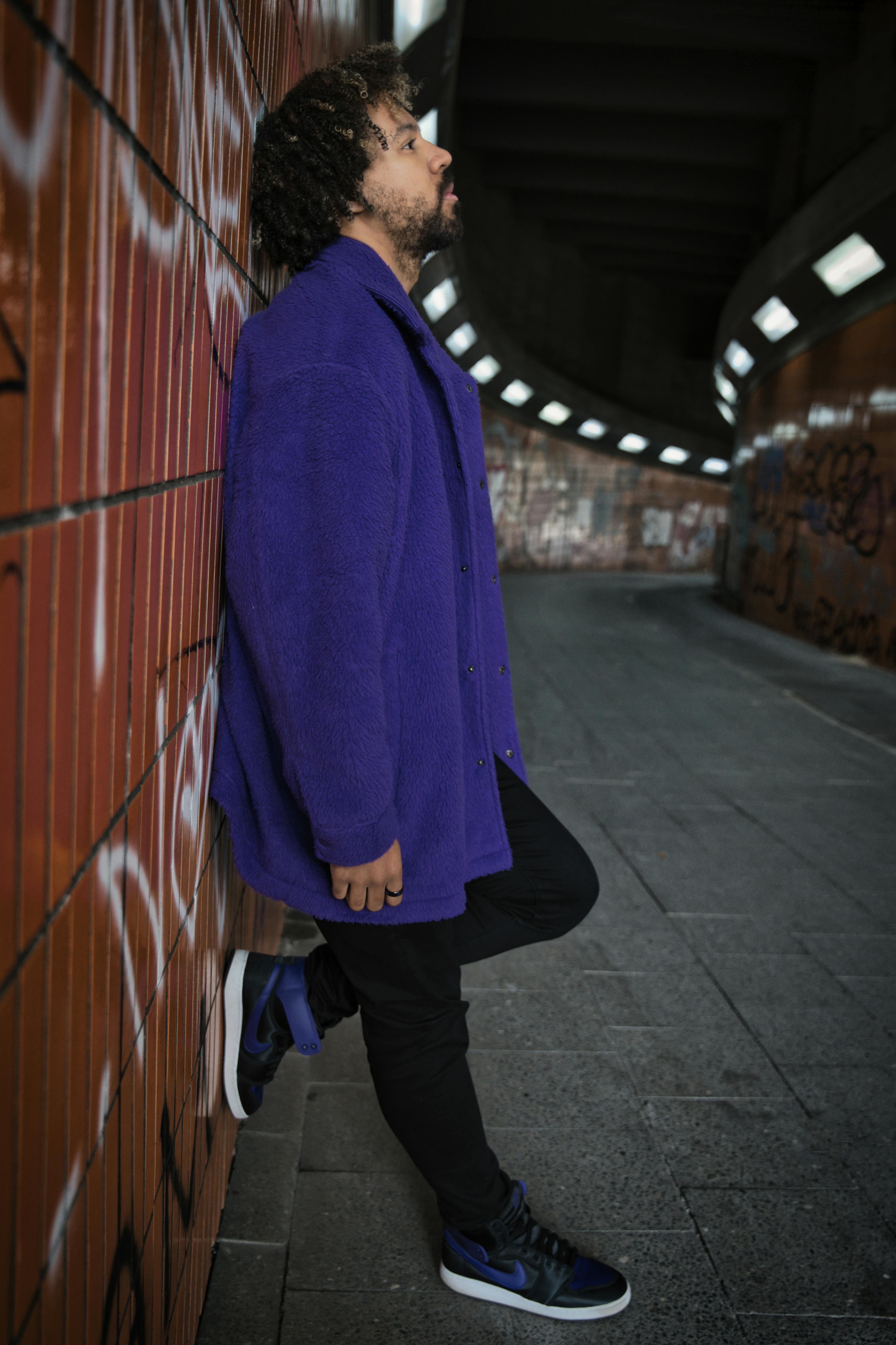 man in purple coat leaning on graffiti wall