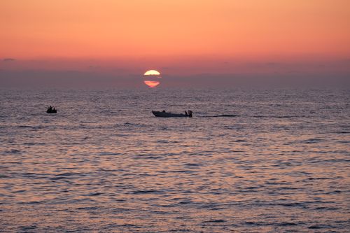Free A serene sunset scene with boats on the horizon over calm ocean waters. Stock Photo