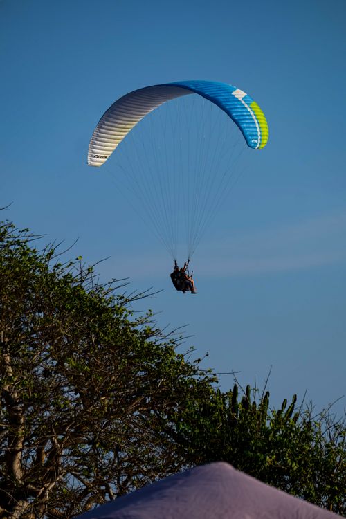 Free Enjoy the thrill of paragliding high above a scenic landscape under a clear blue sky. Stock Photo