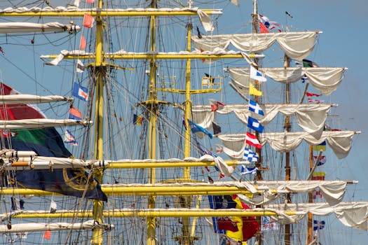 Colorful tall ship masts with unfurled sails and flags against a clear sky.