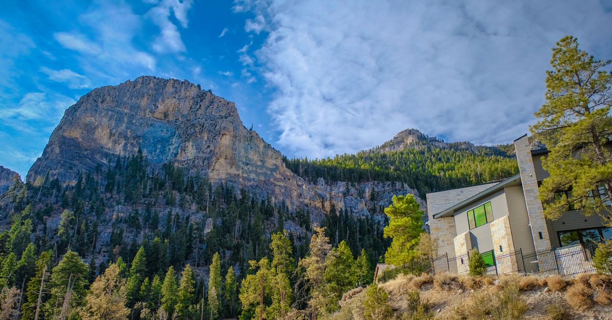 Scenic view of a towering mountain beside a modern house under a blue sky.