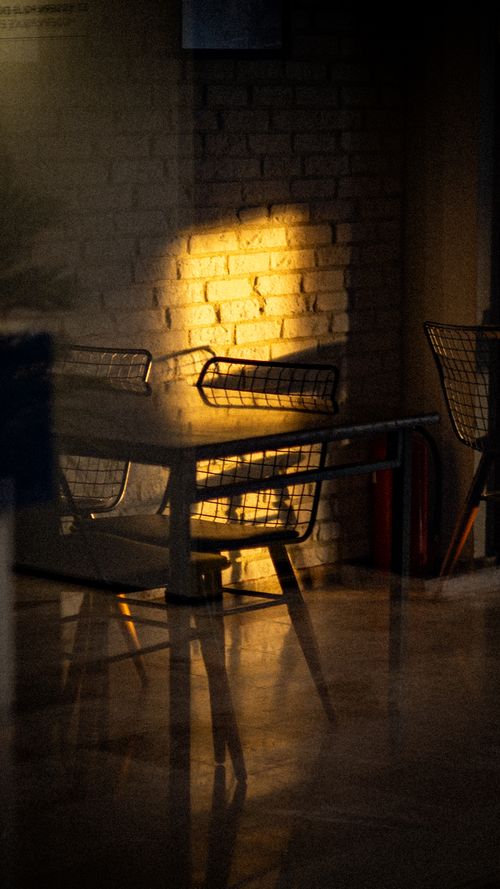 Free Moody cafe setting with chairs and sunlit brick wall casting dramatic shadows. Stock Photo
