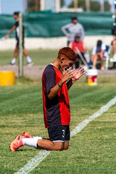 Soccer player kneeling on the field, expressing emotion during daytime match.