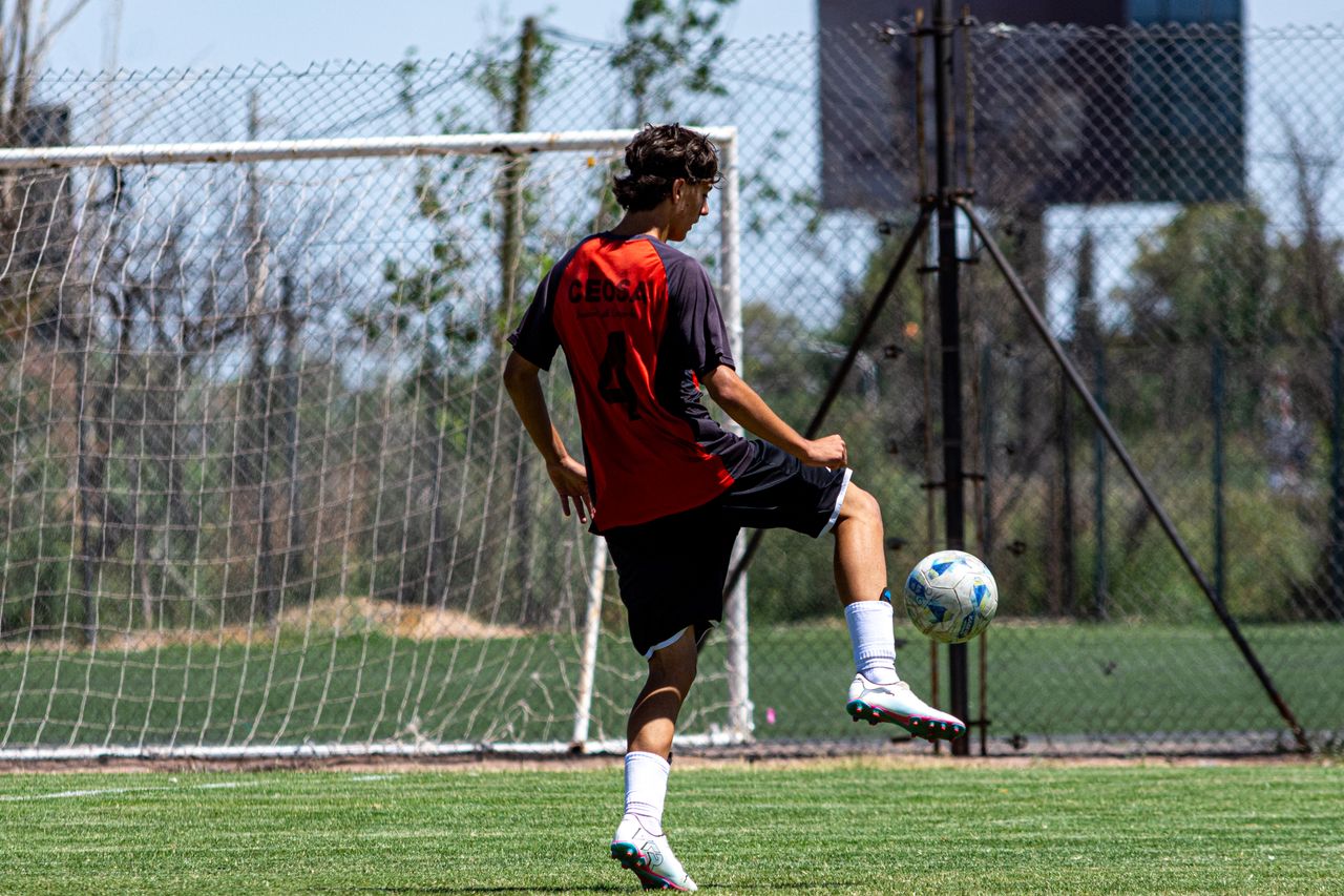 teenager in red jersey playing soccer on an outdoor field during dayti