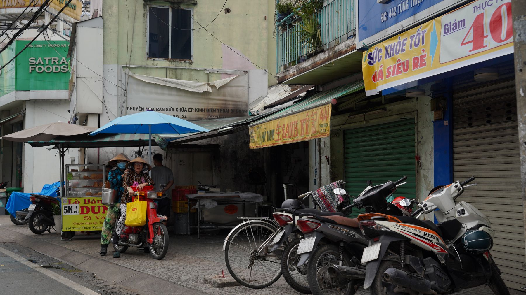 Vibrant street view featuring motorbikes, market stalls, and traditional architecture in an urban setting.