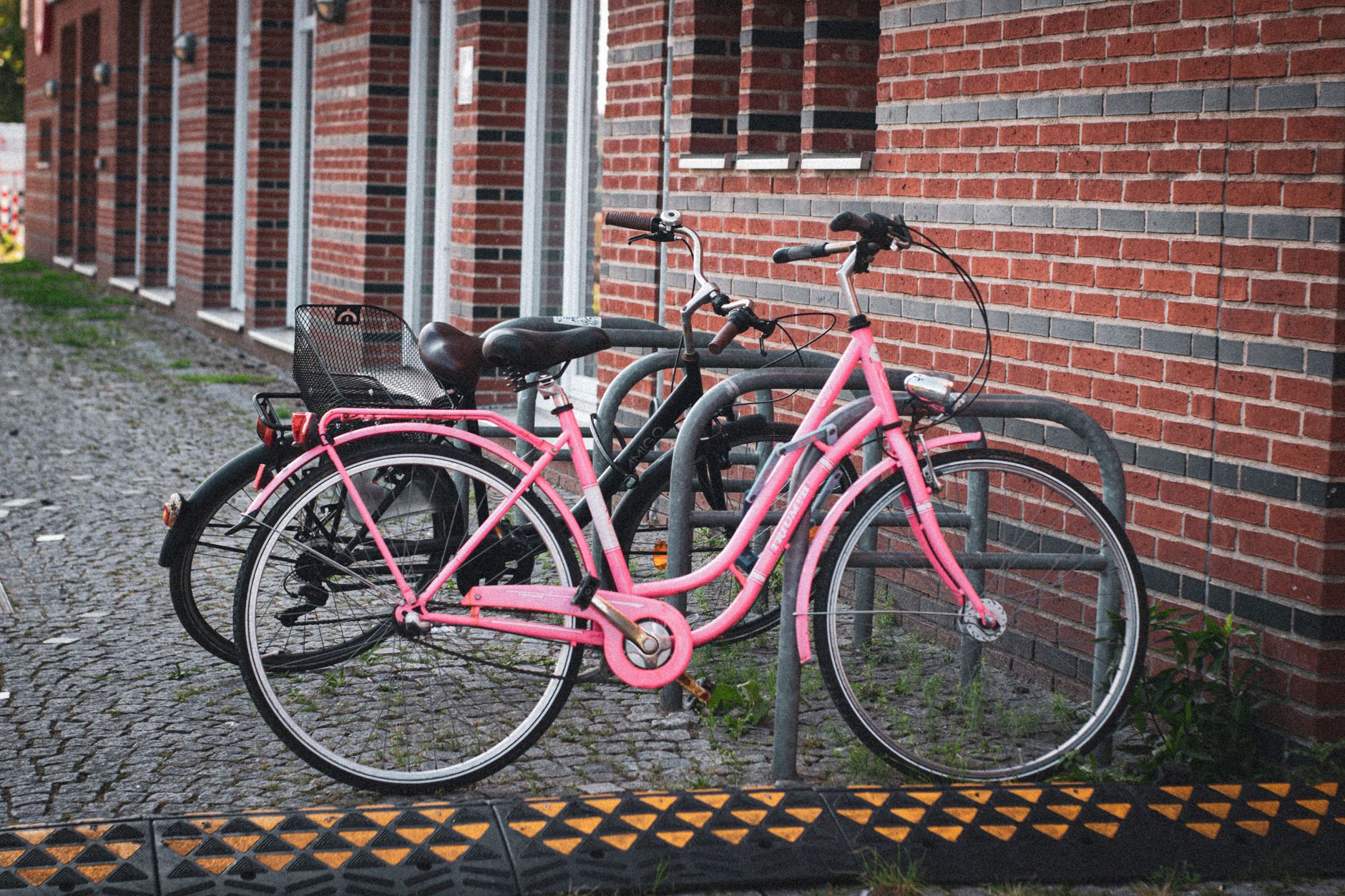 Two bicycles, one bright pink, parked in front of brick wall in Bremen, Germany.