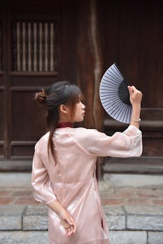 Young woman in traditional attire holding a folding fan outdoors.