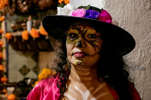 Free Woman with intricate Day of the Dead makeup and floral hat in a festive setting. Stock Photo
