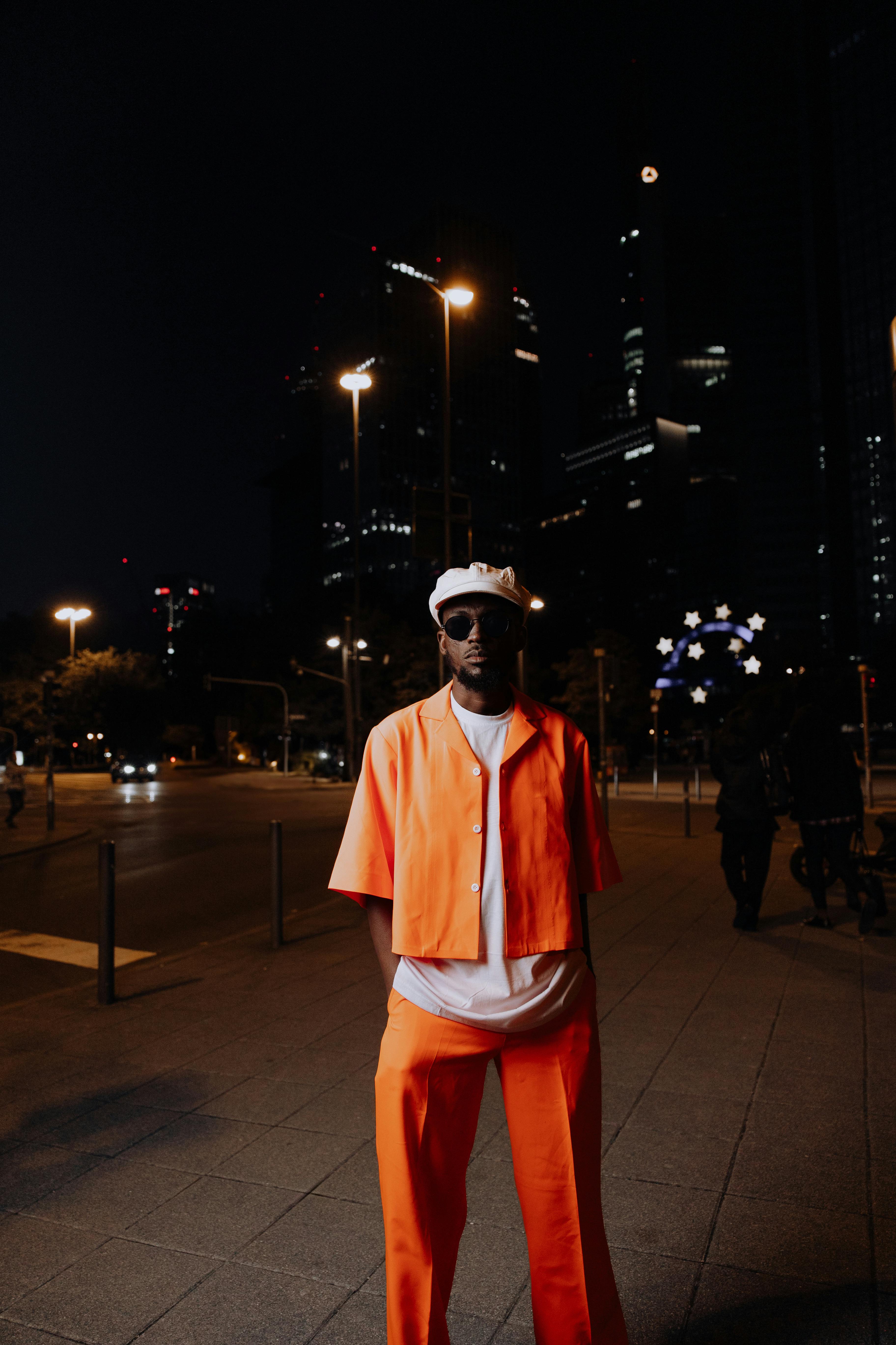 stylish man in orange outfitted stands in frankfurt at night