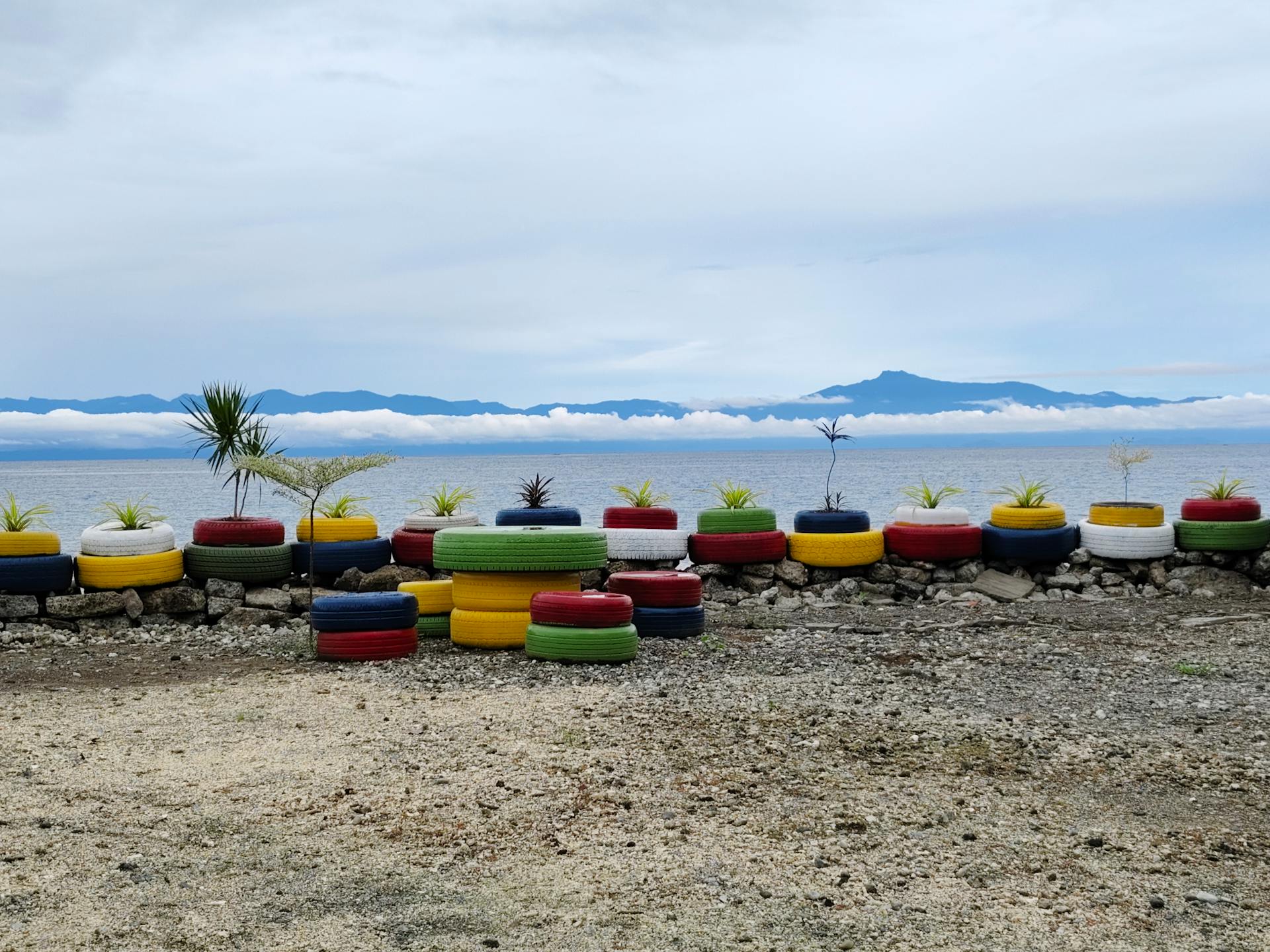 Vibrant upcycled tire planters positioned by a tranquil lakeside view, showcasing sustainable gardening.