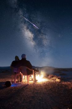 Couple enjoying a campfire under the Milky Way in Iran with a shooting star in view.