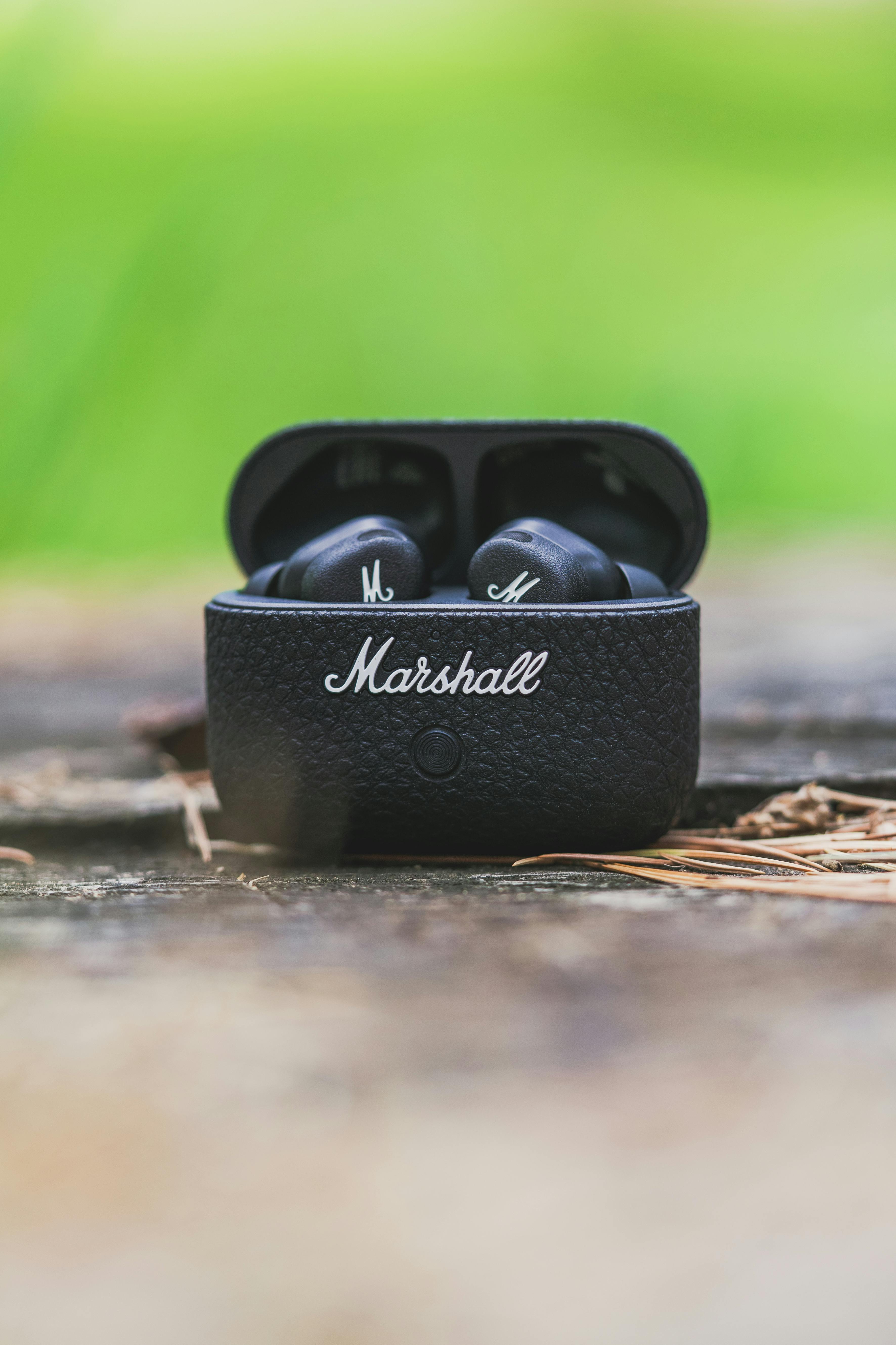 Close-up of Marshall earbuds in black case placed outdoors on a wooden surface.
