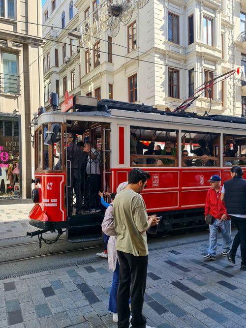 Free Iconic red tram traversing a lively city street with pedestrians and historic buildings. Stock Photo