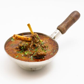 Flavorful Indian mutton curry served in a traditional steel pan, perfect for authentic dining experiences.