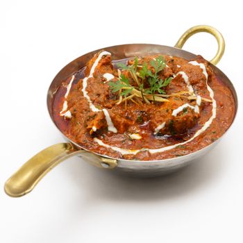 A flavorful Indian curry garnished with cilantro in a traditional brass kadhai.