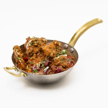Delicious spicy Indian chicken curry served in a traditional brass pan with garnishing.