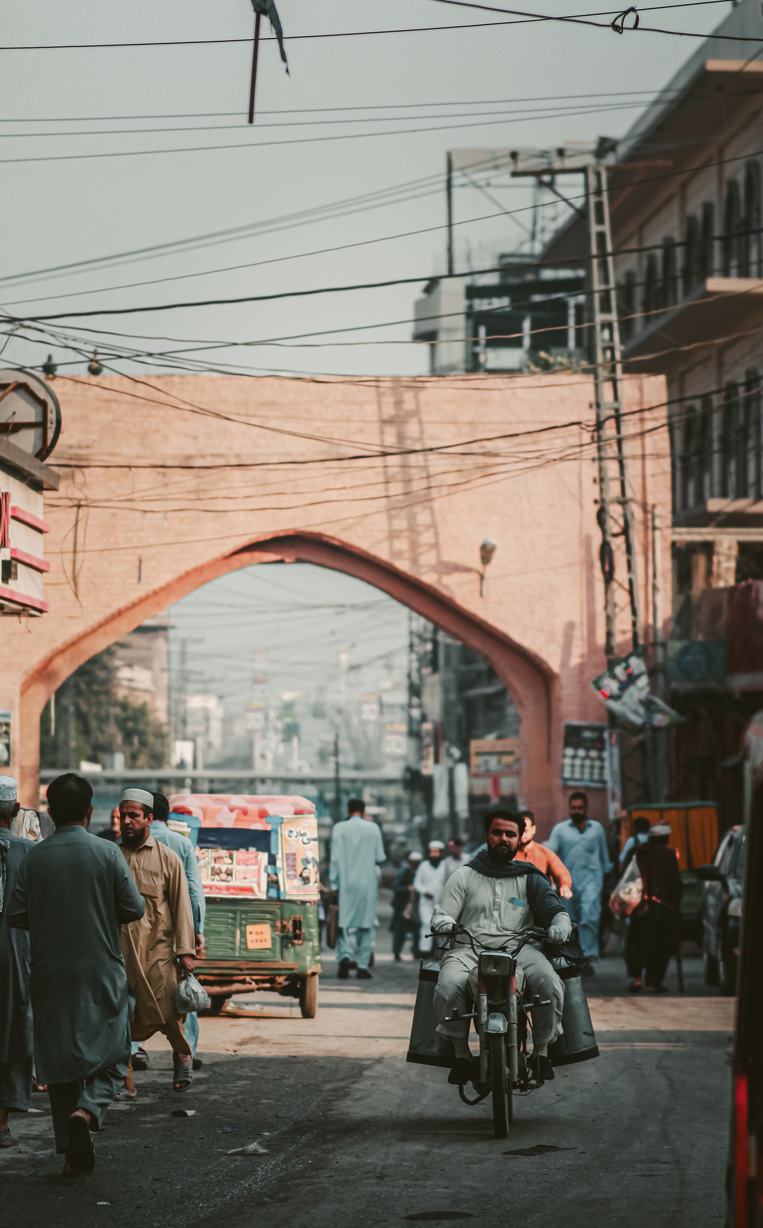 A vibrant street scene in Pakistan featuring a motorcycle rider passing through a bustling intersection.