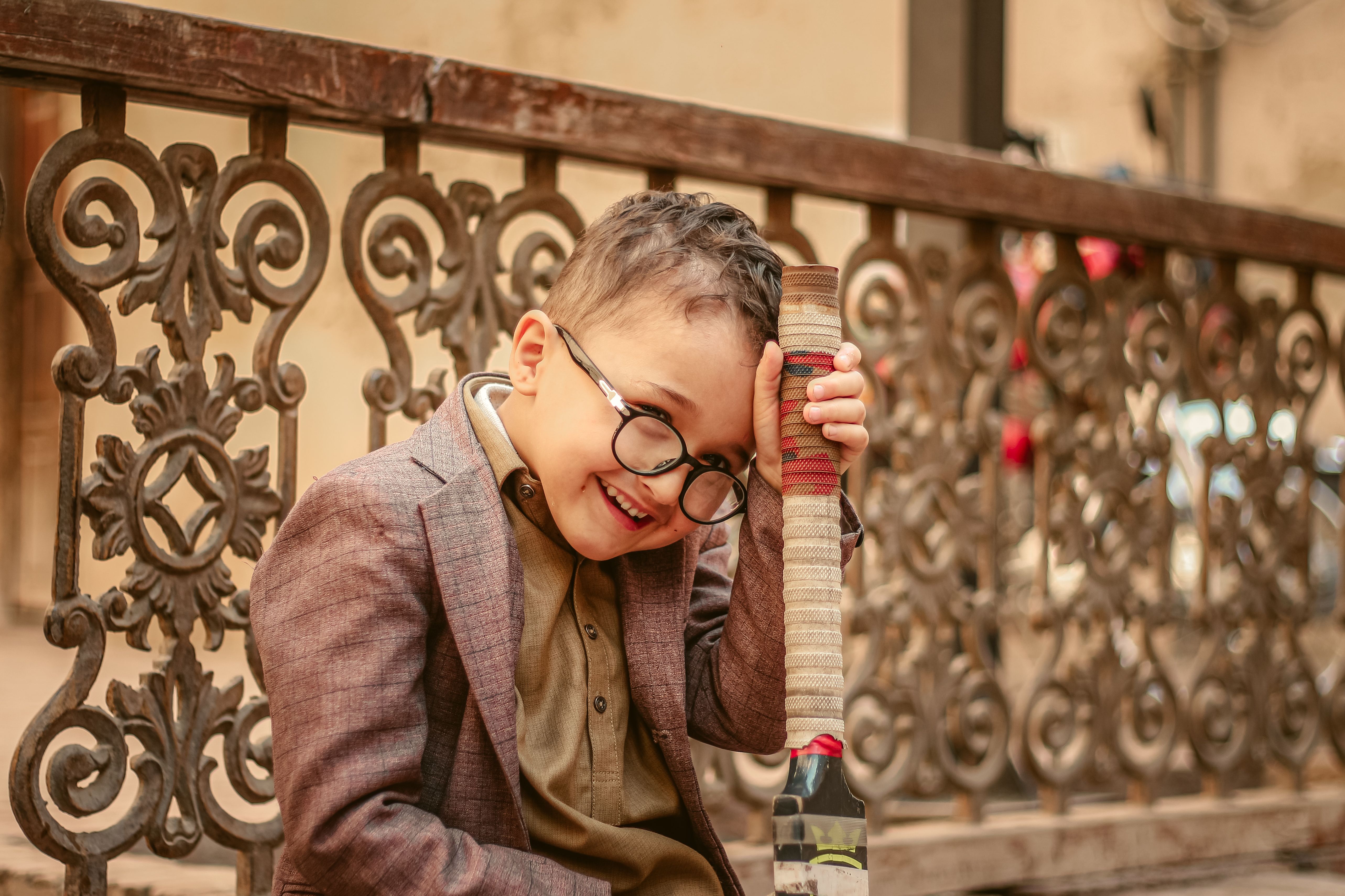A joyful child with glasses wearing a brown suit, holding a toy in an outdoor setting.