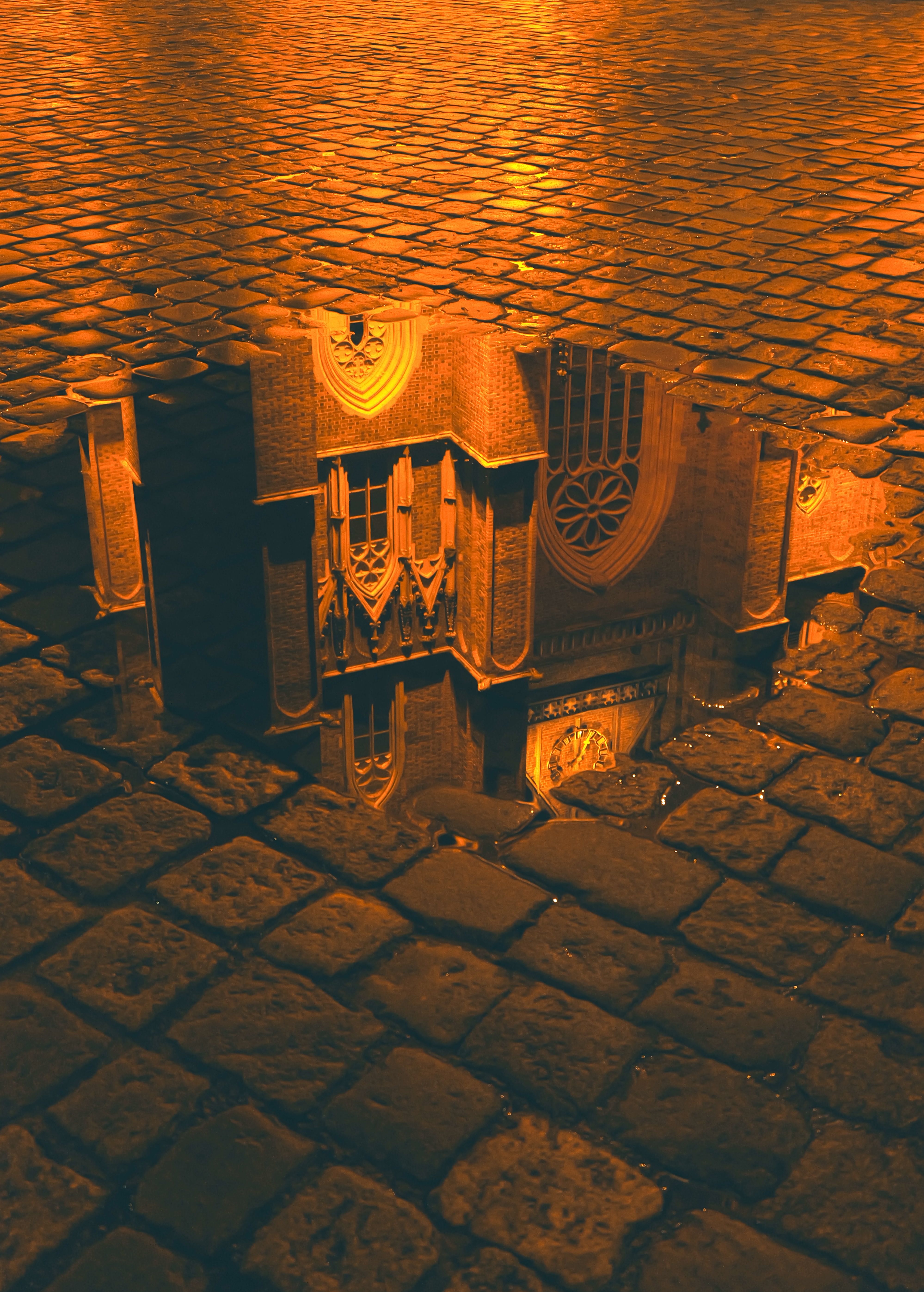A detailed reflection of an ornate building in a puddle on a cobblestone street at night.
