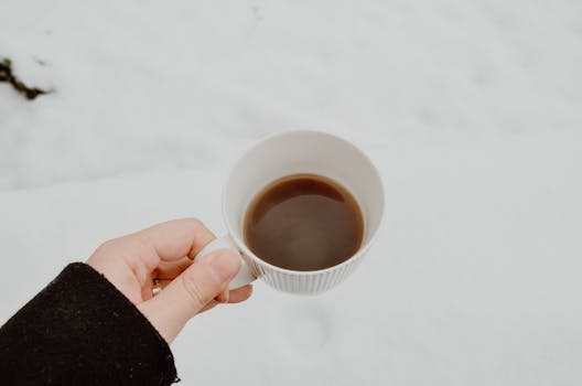 A hand holding a mug of coffee in the snow, capturing a cozy winter moment.