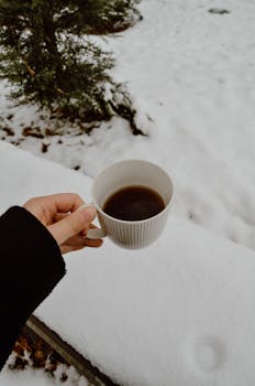 A person holding a coffee mug against a snowy backdrop, epitomizing winter coziness.