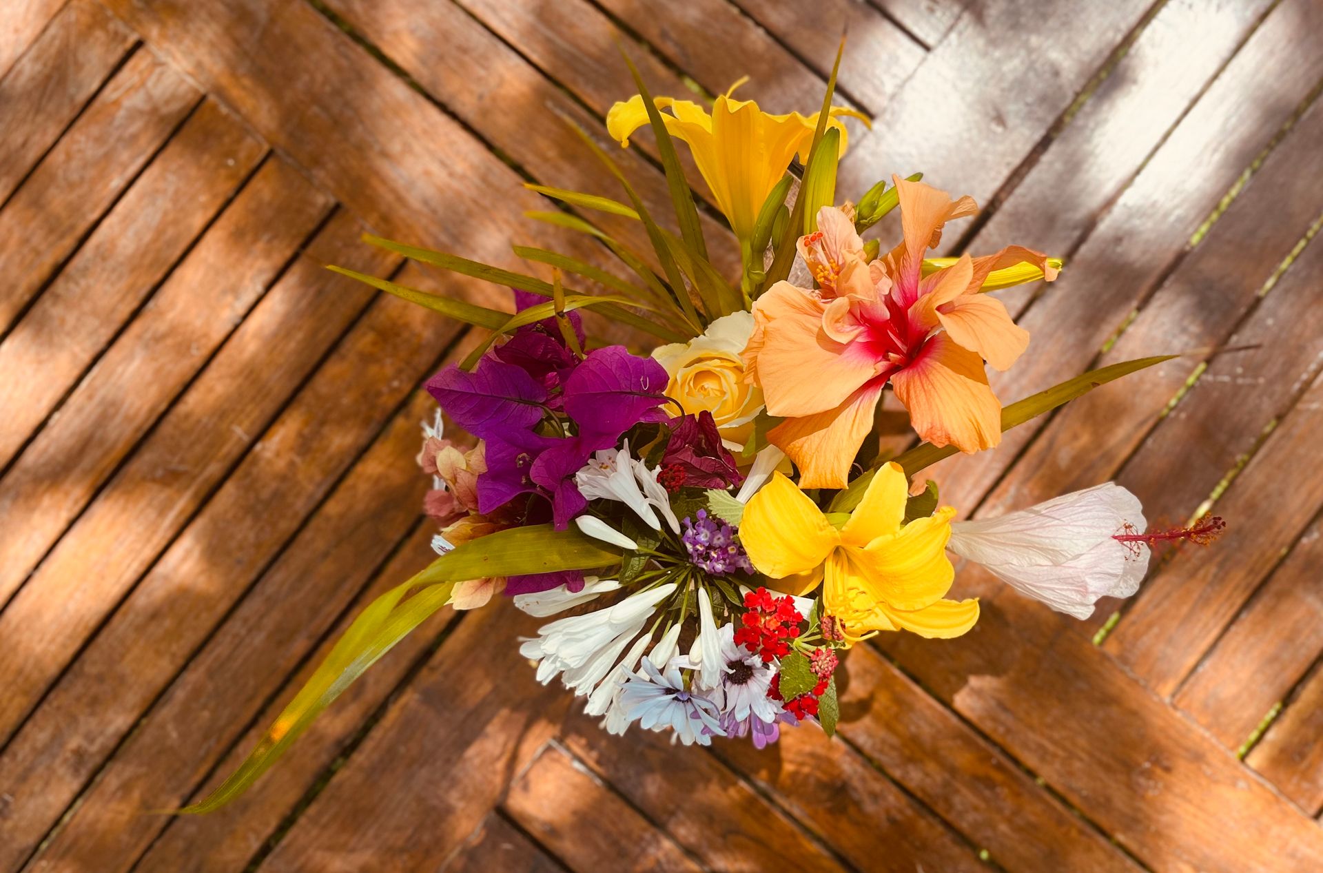 A colorful bouquet of tropical flowers displayed on a wooden table in natural daylight.