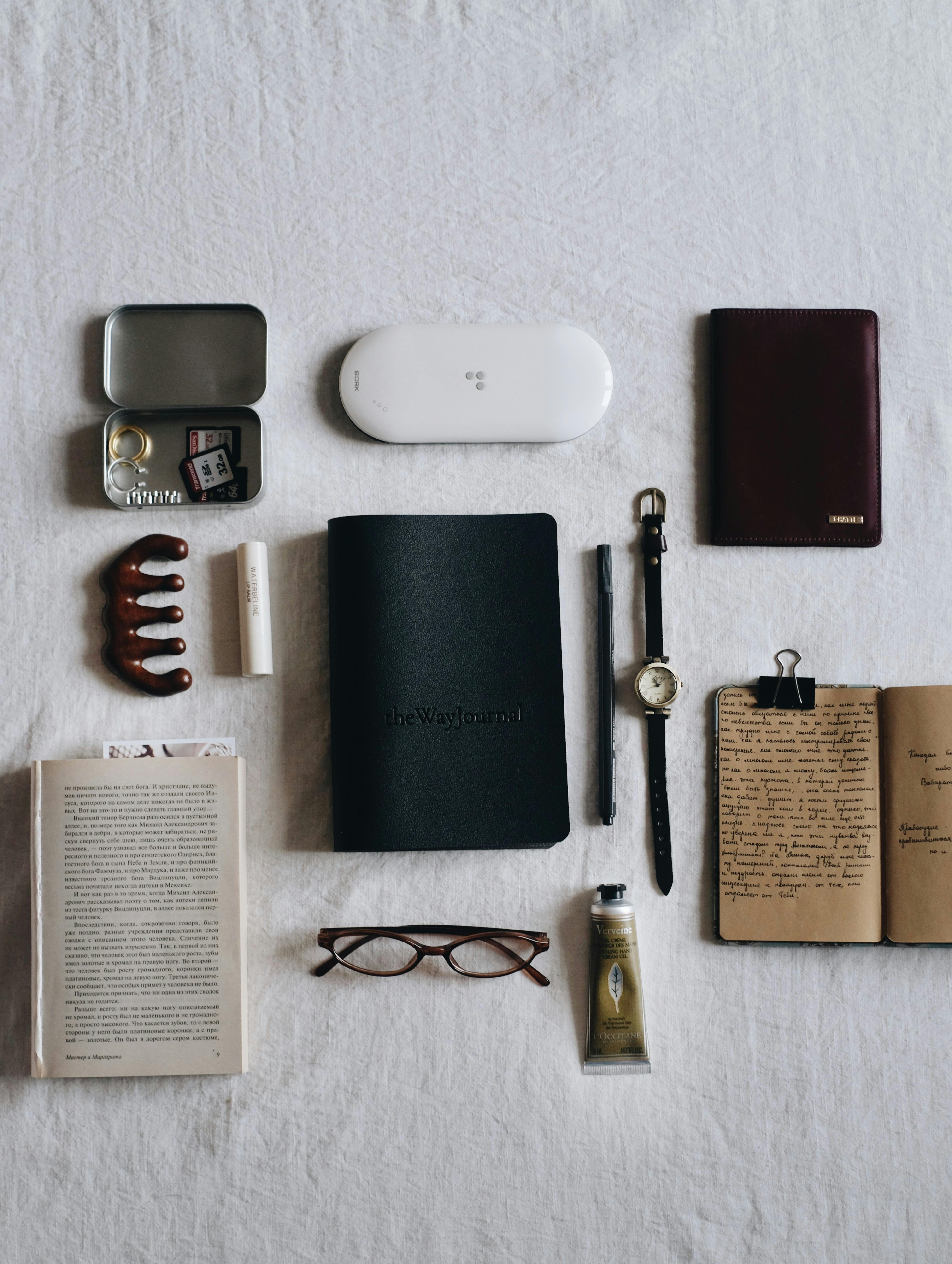 Stylish flat lay with watch, notebook, glasses, and journal on white fabric.