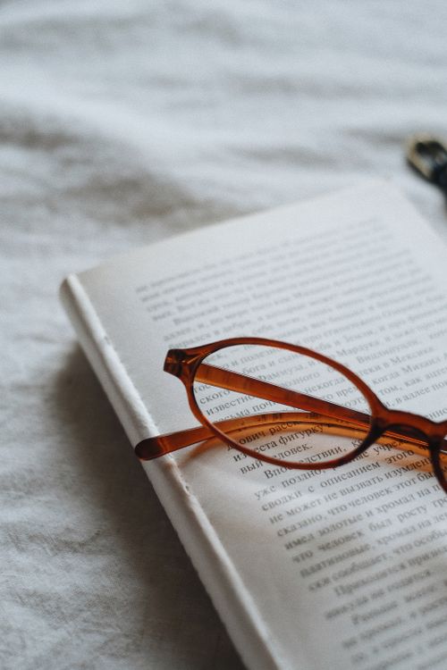 Free Brown glasses resting on an open book with text, cozy indoor setting. Stock Photo