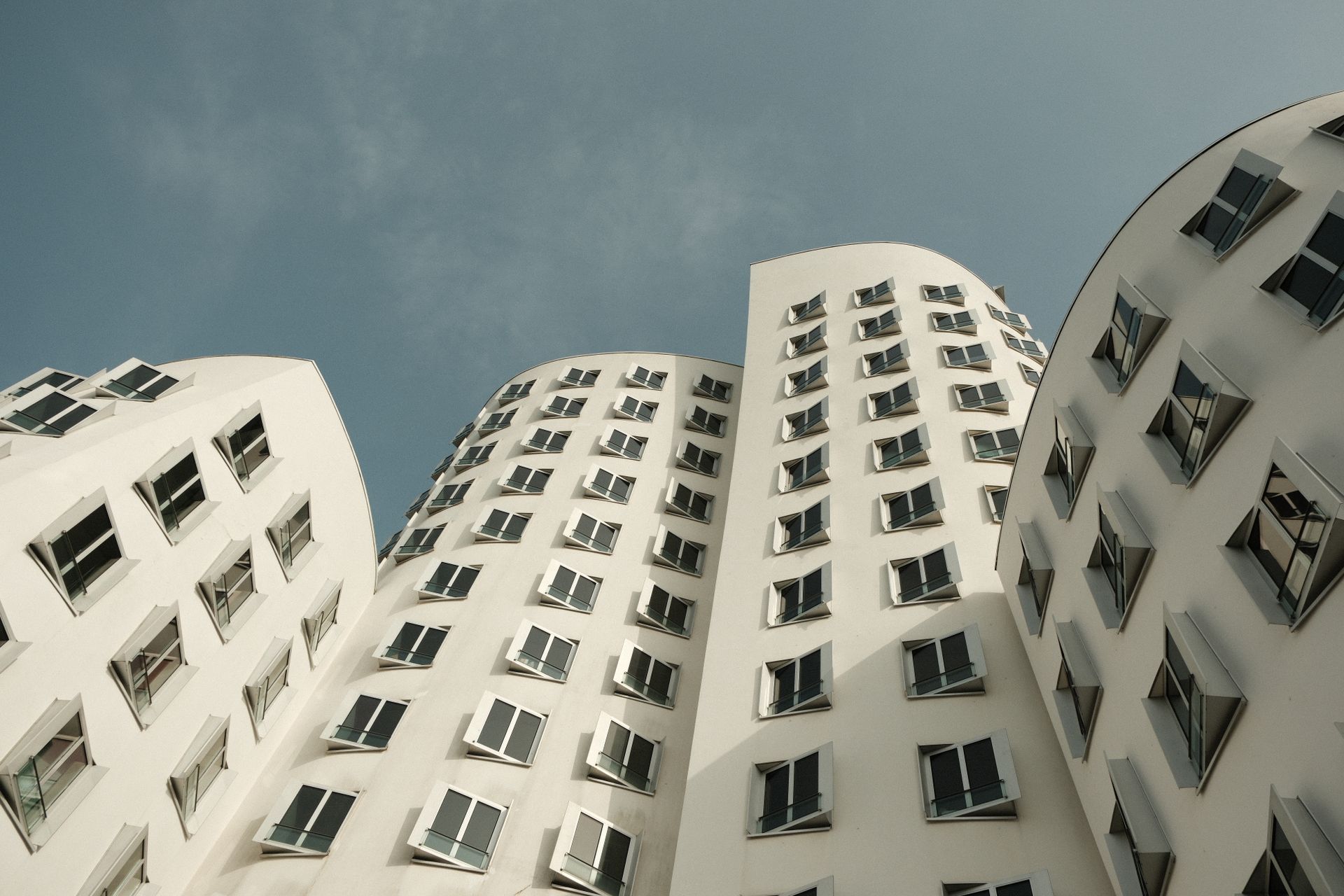 Modern architectural design of Gehry buildings in Düsseldorf, Germany. Unique white facade against a clear sky.