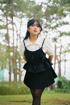 Young woman in black dress poses in a serene forest, showcasing a modern fashion style.
