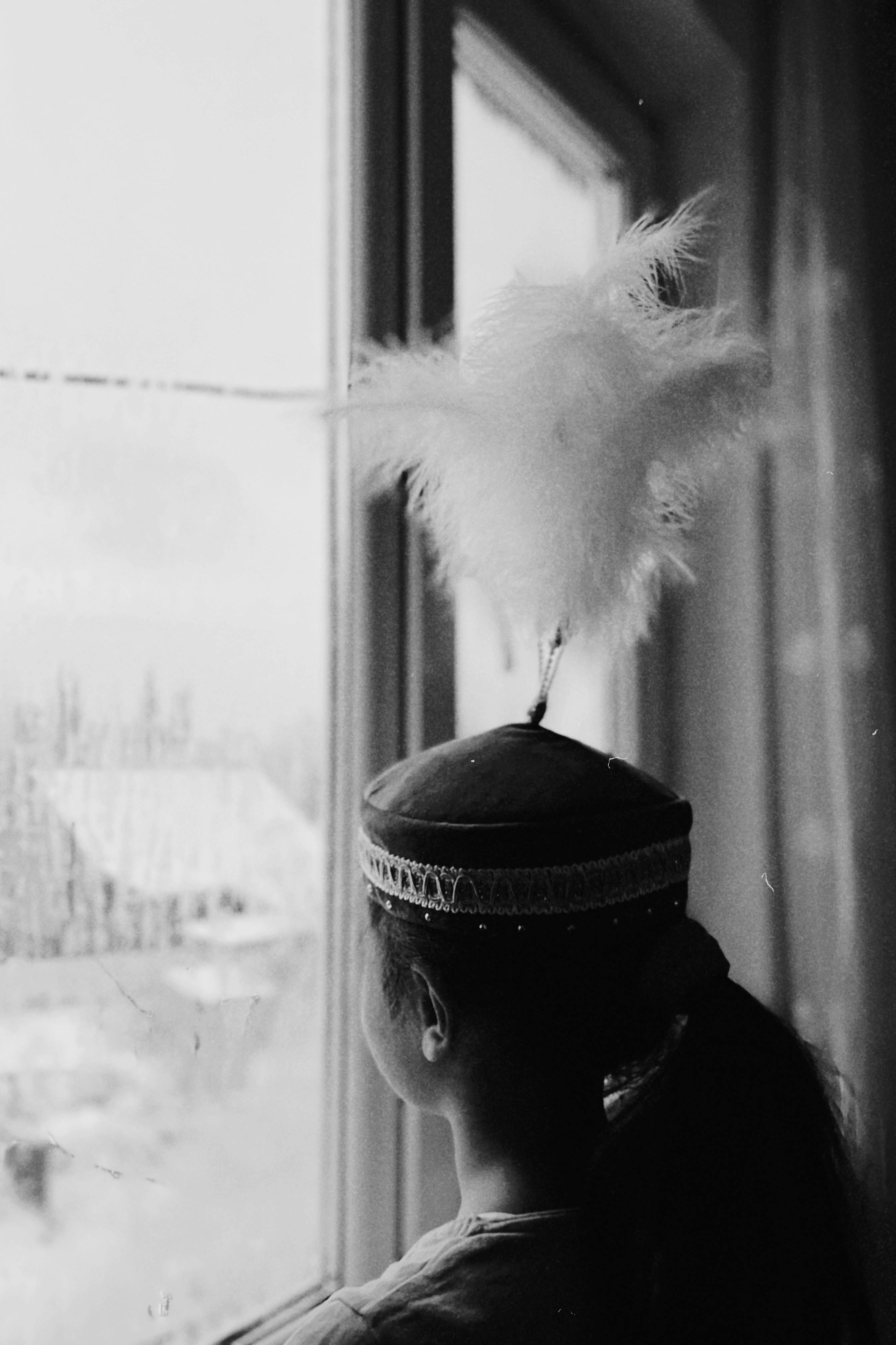 A girl in a traditional feathered hat looks out at a snowy scene in Talgar, Kazakhstan.